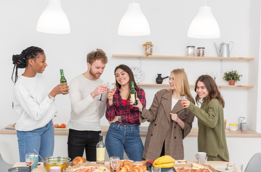 Casual entertaining at home illustrated through friends sharing food and drinks in kitchen.
