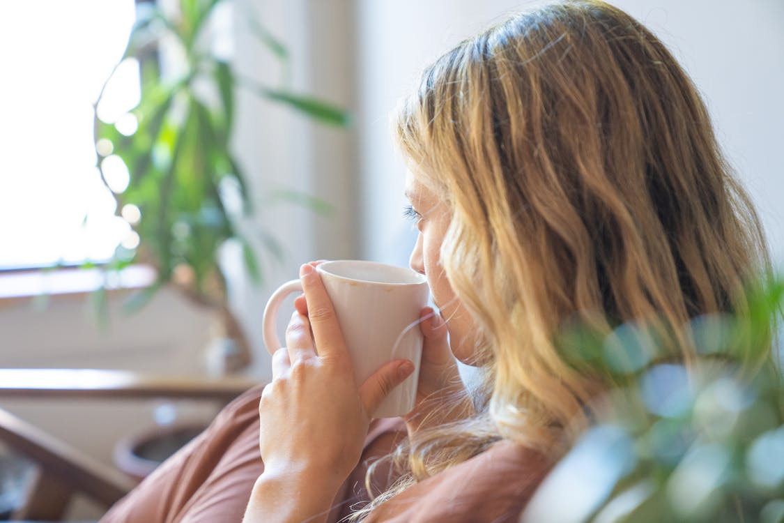 Woman drinking coffee by a window illustrating a calming morning routine.