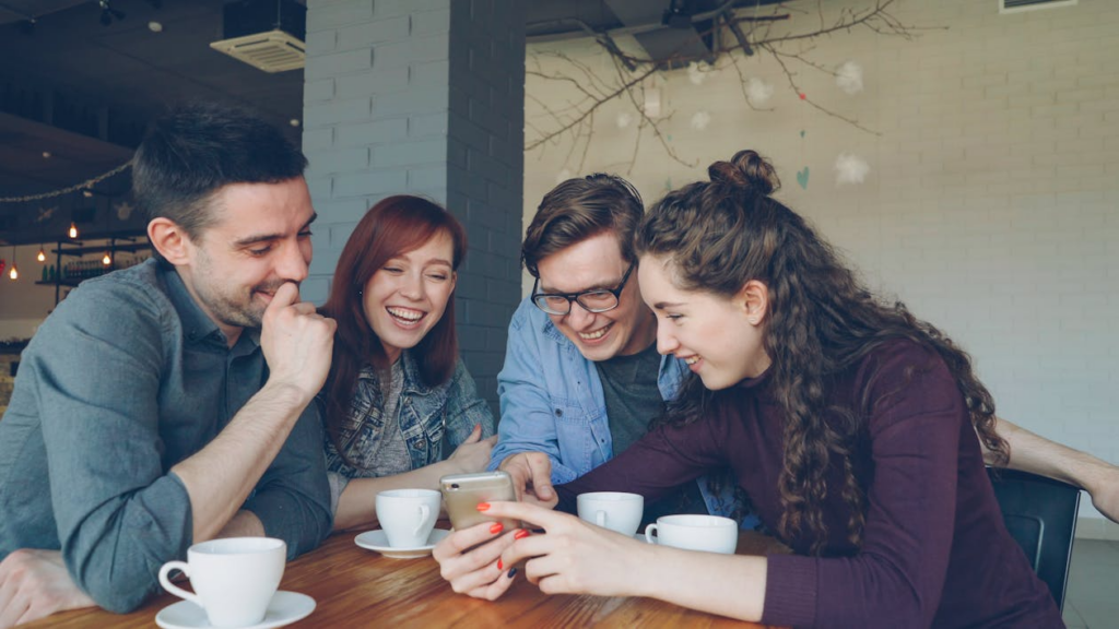 Modern friendship rituals shown through friends sharing coffee and looking at a phone together.