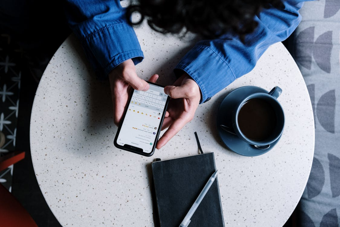 Group chat etiquette shown through someone texting on a phone beside coffee and a notebook.