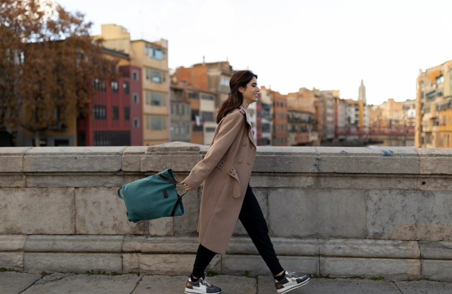Practical fashion trends shown through a woman walking in sneakers, a long coat, and everyday bag.