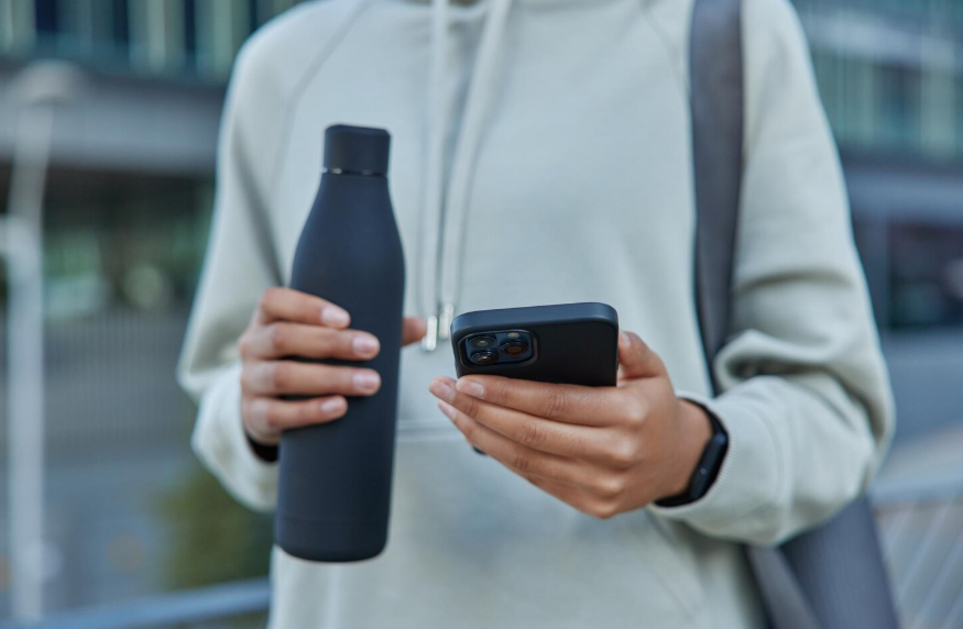 Modern status symbols shown through a person holding a reusable water bottle and smartphone.